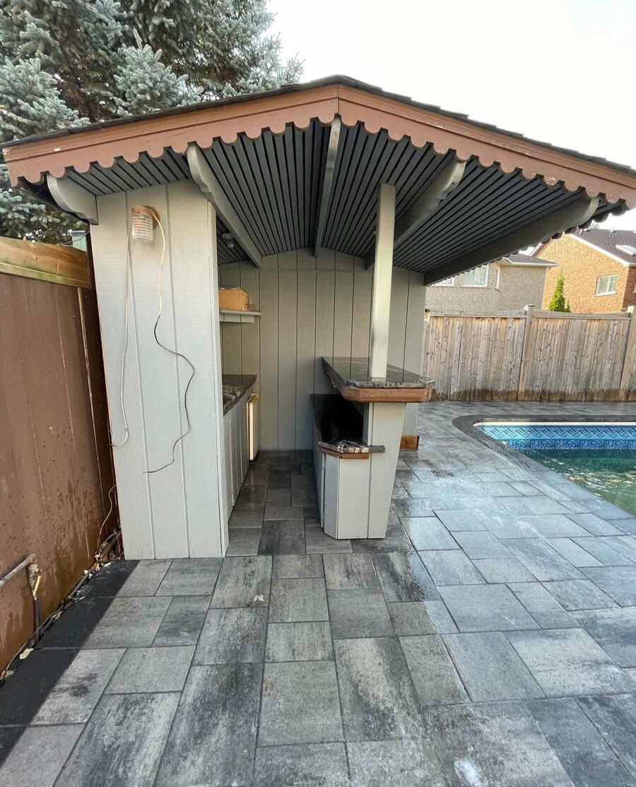 Backyard bar and cabana sitting on interlock pad near pool.
