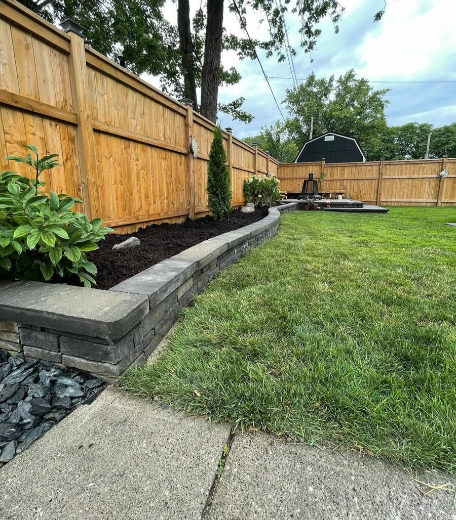 Low retaining wall with raised garden bed and fresh sod.