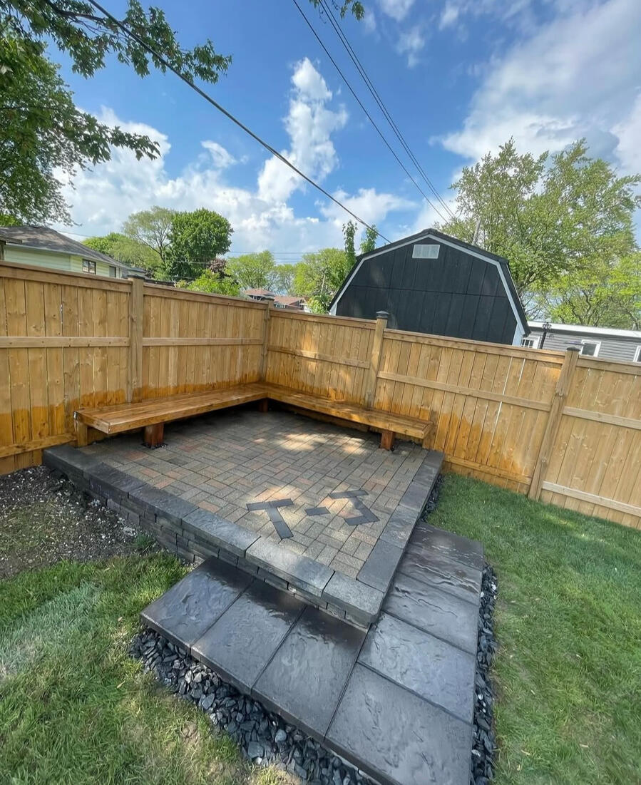 Corner interlock patio with built-in wooden bench along fence.